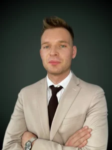 Abraham Sieniawski prawnik w beżowym garniturze z krawatem i założonymi rękoma na szarym tle
