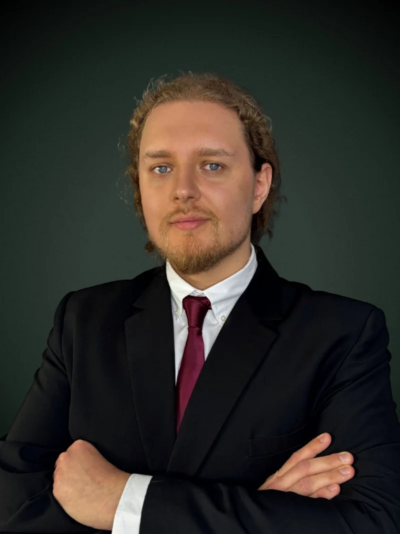 Marcin Popielarz analityk w czarnym garniturze z bordowym krawatem na ciemnym tle