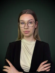 Martyna Zahraj konsultant w czarnej marynarce i okularach z założonymi rękoma na ciemnym tle