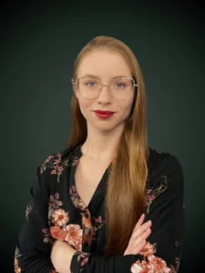 Natalia Szostek konsultant w czarnej marynarce z kwiecistym wzorem i okularach na szarym tle