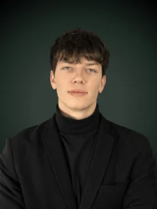 Bartosz Wach konsultant ds. usług prawnych w czarnej marynarce i czarnym golfie na ciemnozielonym tle, Franki Kancelaria odzyskujemy kredyty CHF i euro