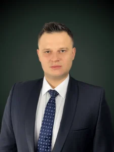 Łukasz Sobolewski radca prawny w granatowym garniturze i czarnej koszuli na ciemnozielonym tle, Franki Kancelaria odzyskujemy kredyty CHF i euro